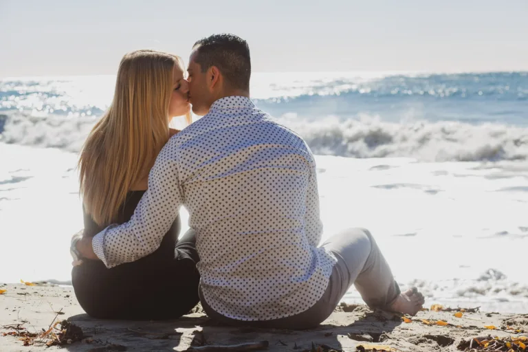 Couple sharing a passionate kiss on a beach in Malibu after getting engaged.