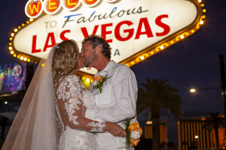 Couple just married at the Las Vegas Sign, sharing a passionate kiss.